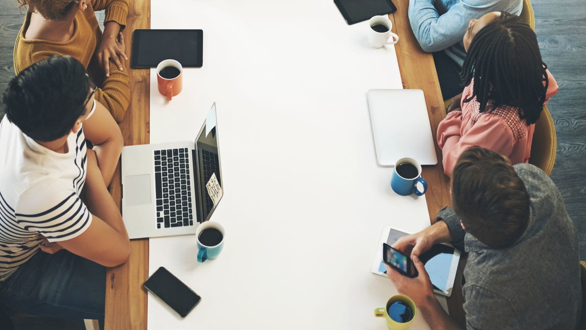 Menschen sitzen am Tisch mit Laptops und Smartphones